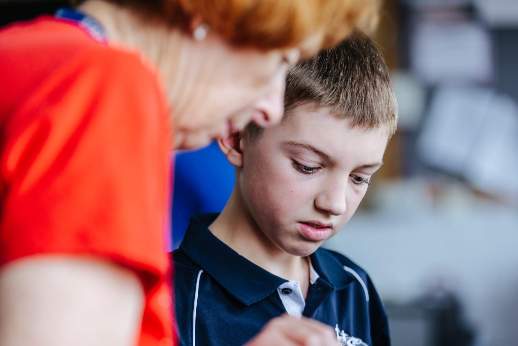 student focusing intently as teacher demonstrates a practical skill in a classroom setting.
