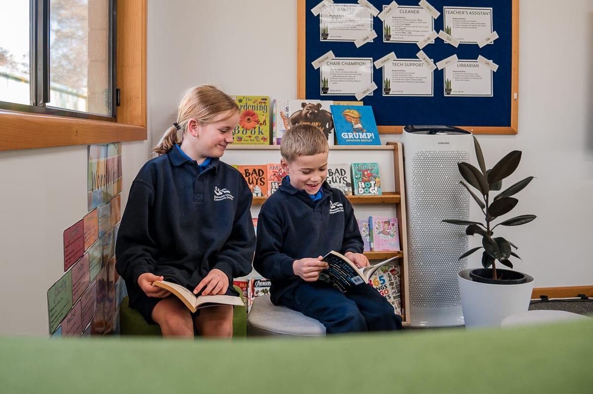 Two primary students reading books together in a school library nook, representing personalised care and a nurturing learning environment where every child is known.