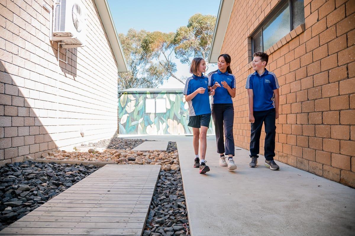 Three upper primary students walking together on campus in conversation, representing student friendship and everyday Christian value.