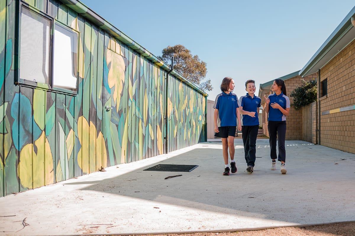 Three students walking together near a vibrant mural, symbolising individuality, friendship, and the nurturing environment where every child is known and valued.