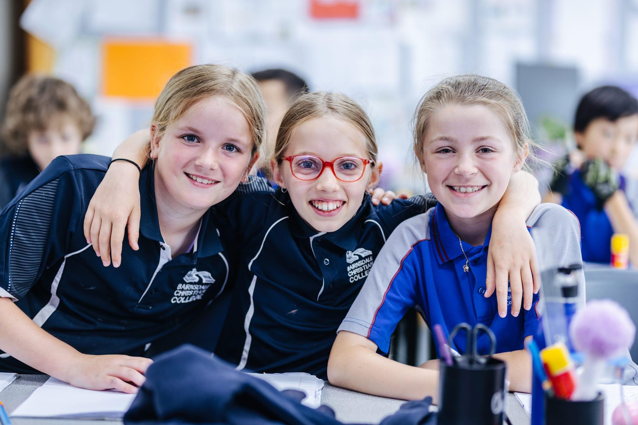 Three upper primary students smiling and embracing in class, celebrating friendship, belonging, and the Christ-like love at the heart of Bairnsdale Christian College.