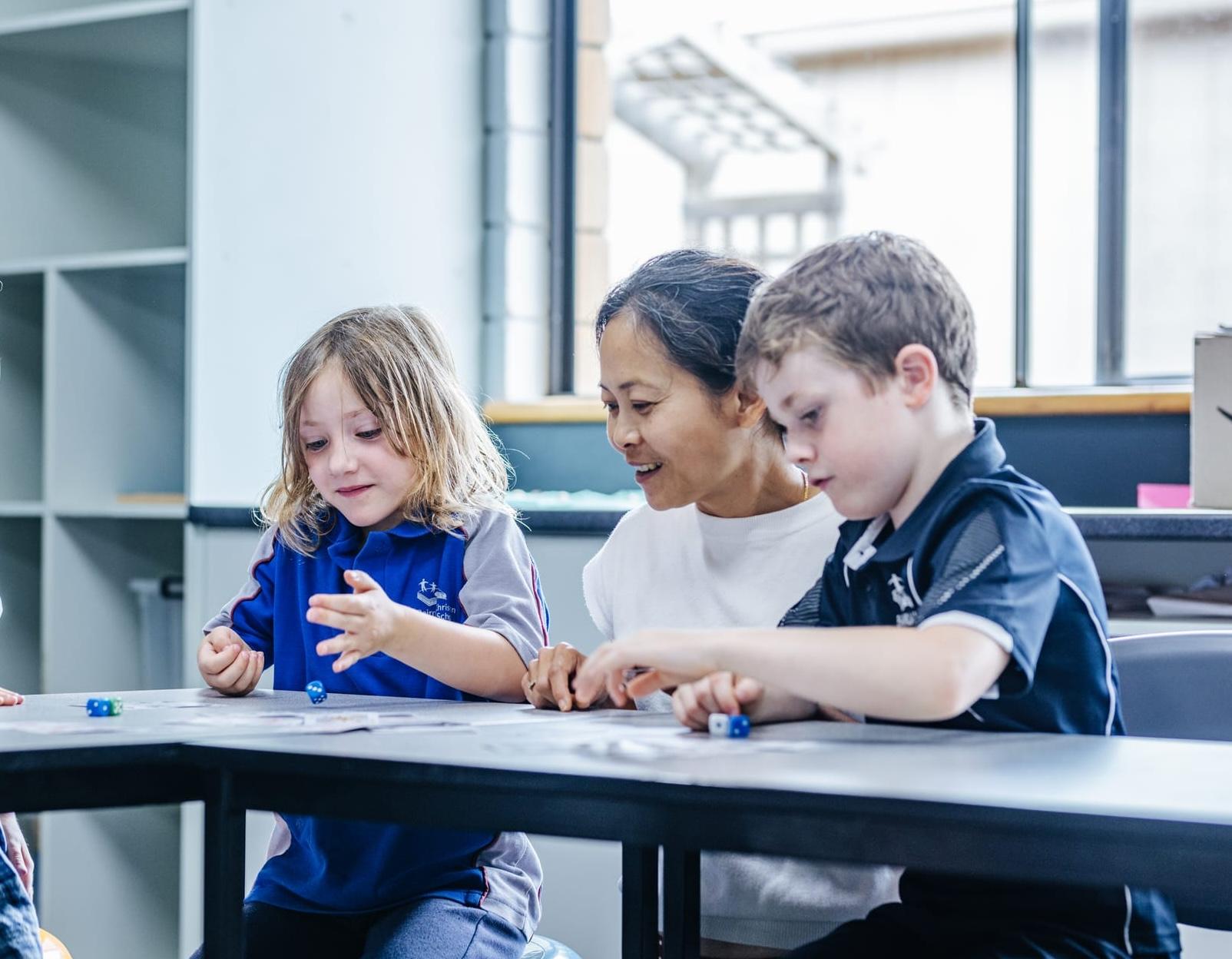 Early primary students learning through play with their teacher, illustrating a nurturing start to education grounded in Christian faith and values.