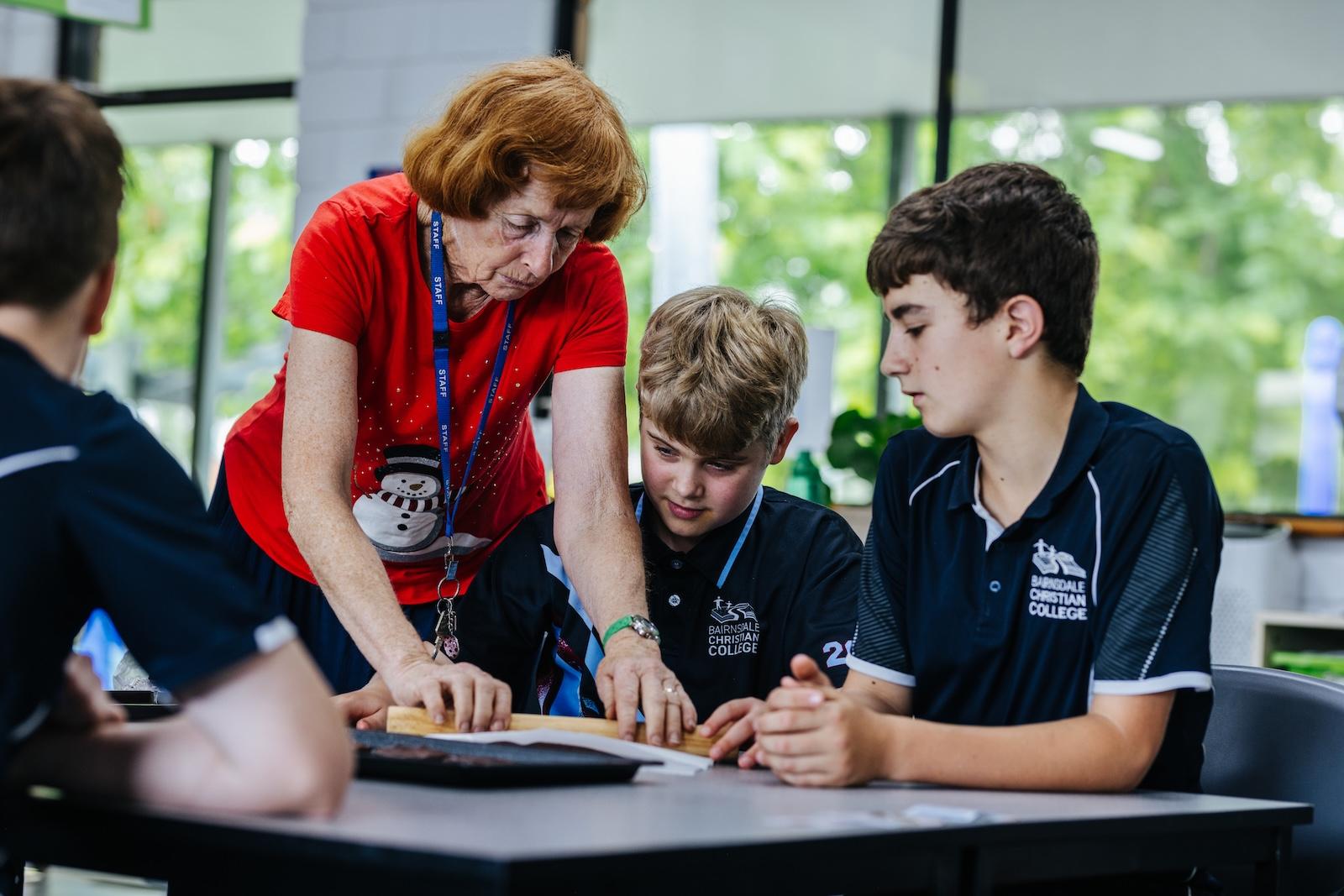 Focused food technology teacher supporting two upper primary students during a practical learning activity at Bairnsdale Christian College.