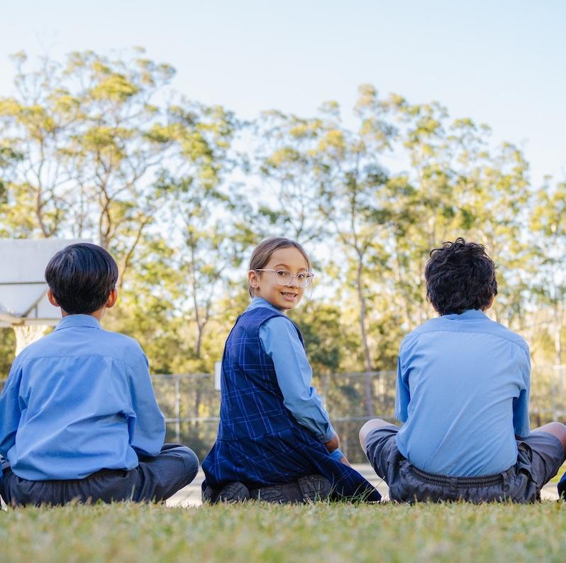 Primary school students seated outdoors on the grass, enjoying a group discussion under clear skies at Medowie Christian School.